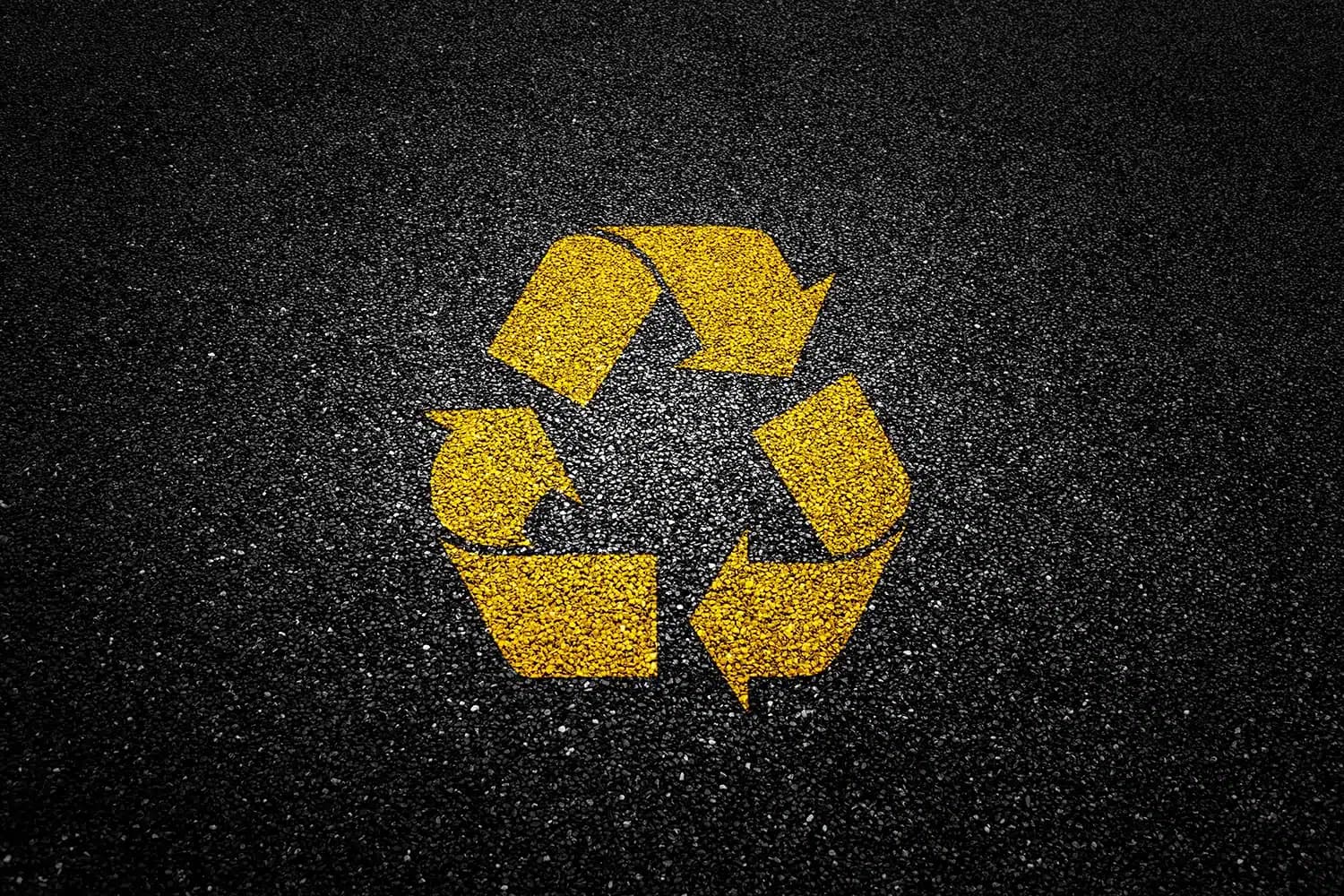 Yellow recycling symbol painted on asphalt pavement