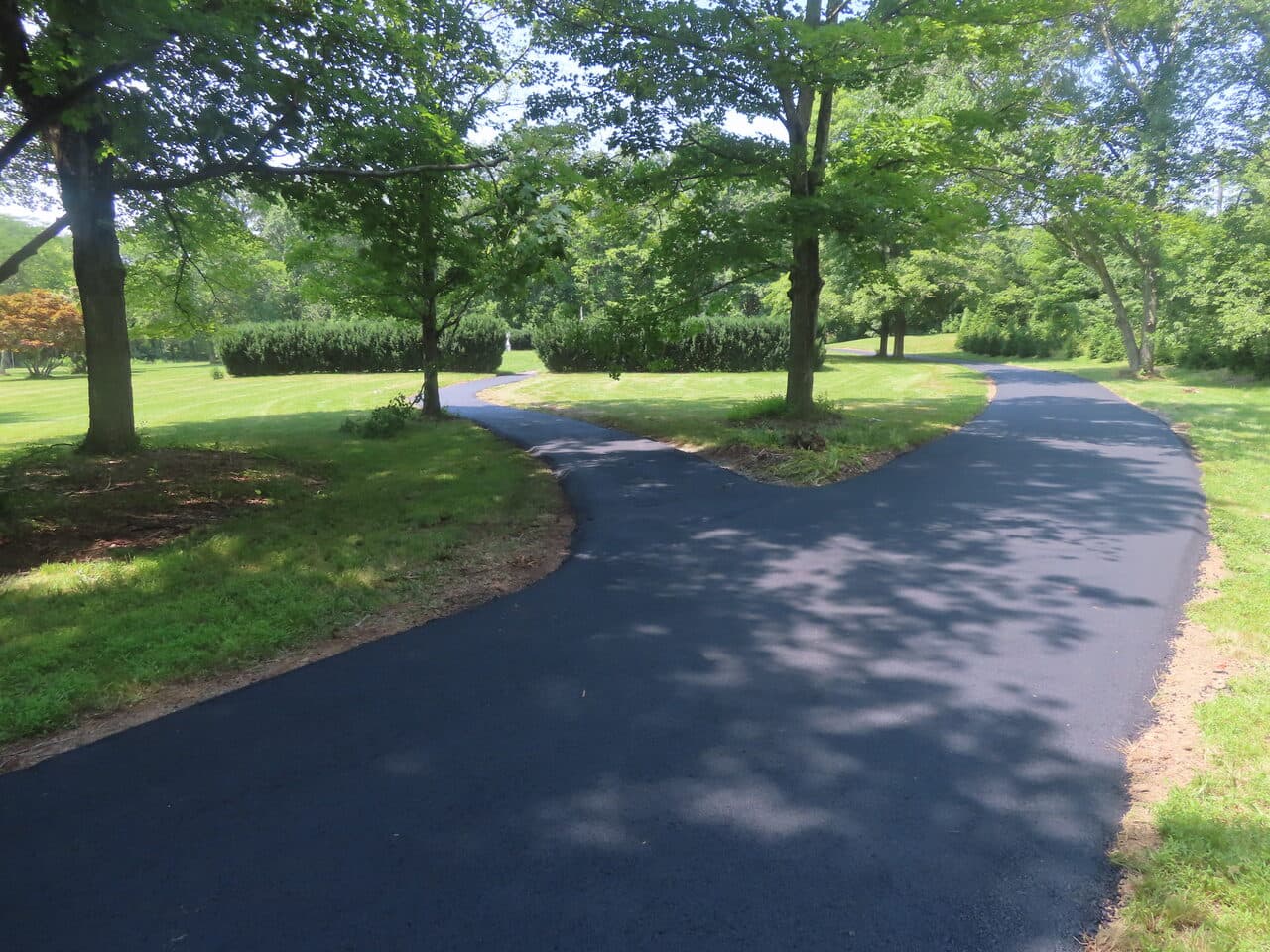 Pedestrian Trail & Parking Lot Paving project in Guilford, CT — fresh paved driveway through trees