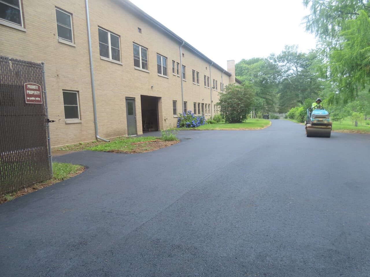 Pedestrian Trail & Parking Lot Paving project in Guilford, CT — roller compacting lot by building