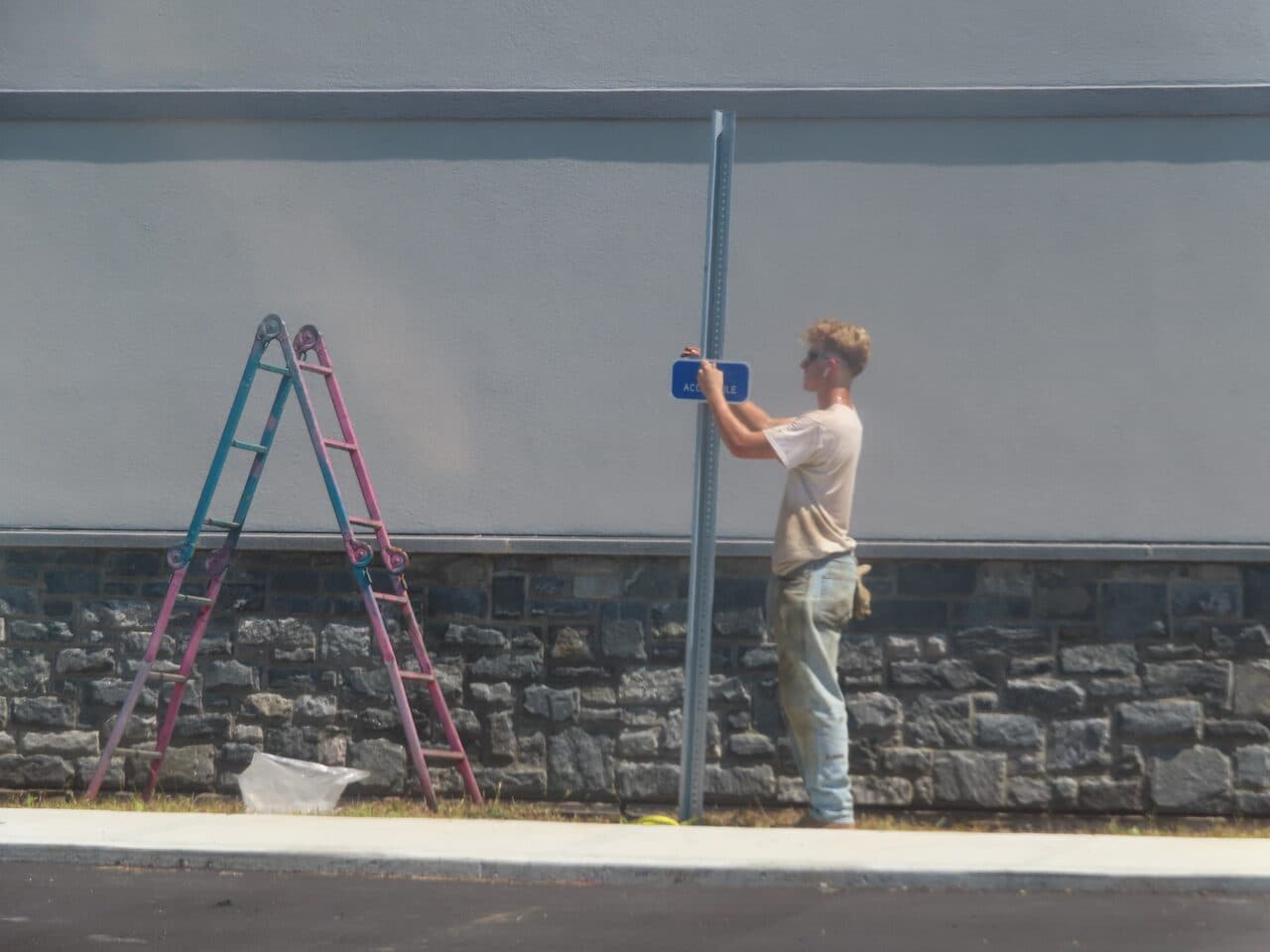Commercial Parking Lot Paving project in Orange, CT — worker installing accessible parking sign