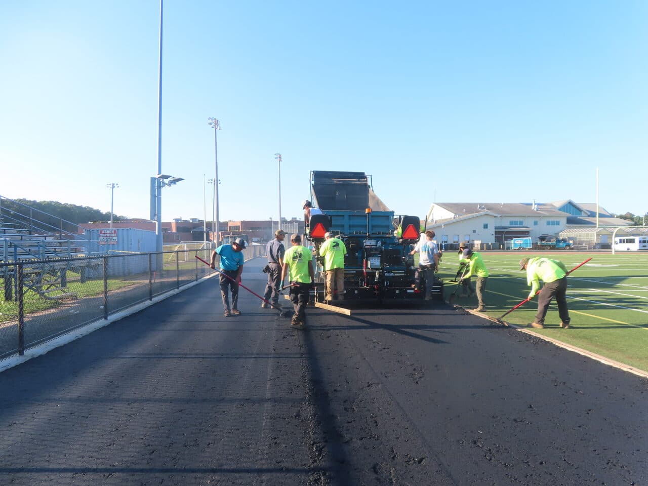 Athletic Surface Base Paving project in Southington, CT — crew raking behind paver