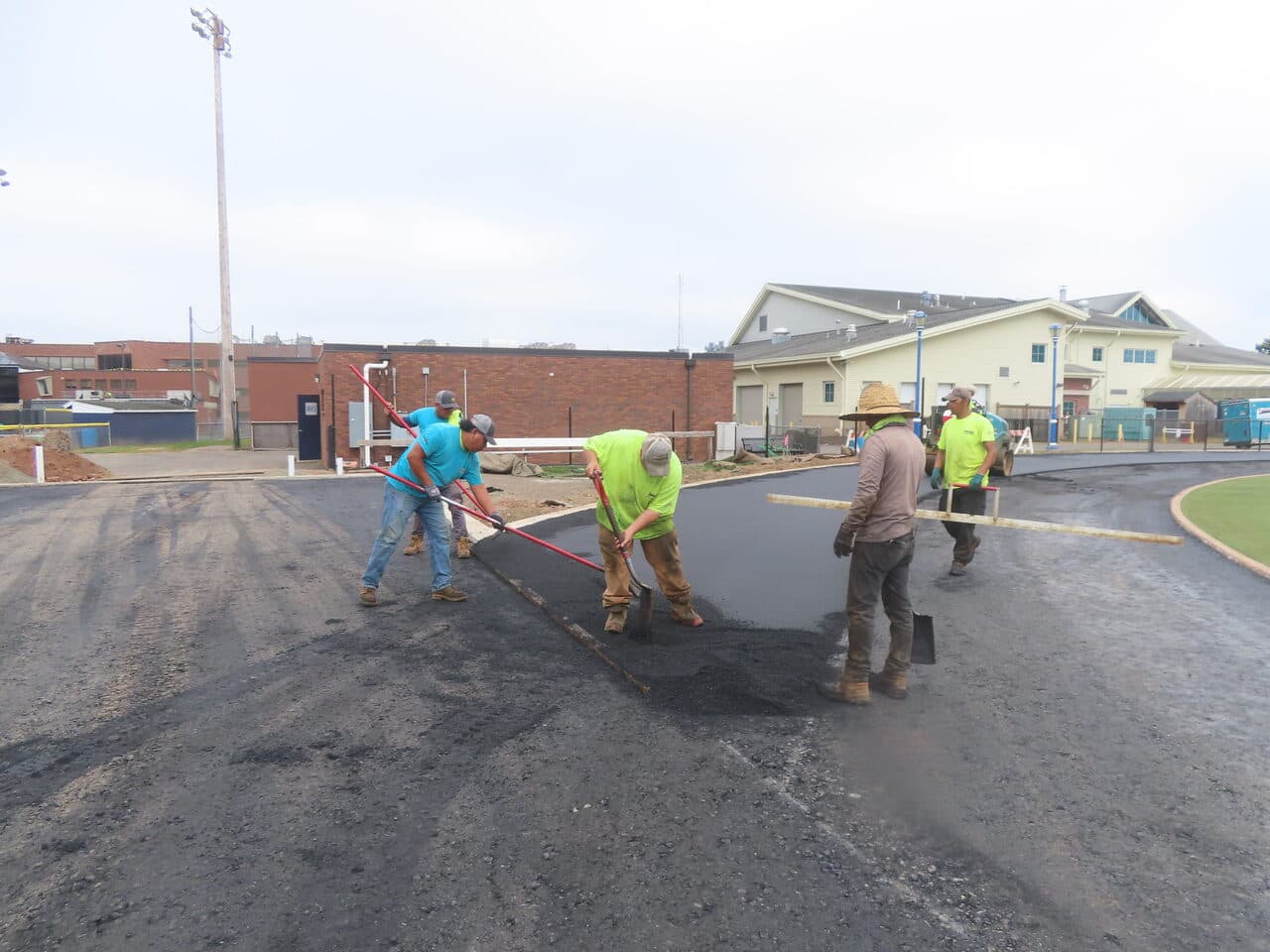 Athletic Surface Base Paving project in Southington, CT — crew handraking asphalt by buildings