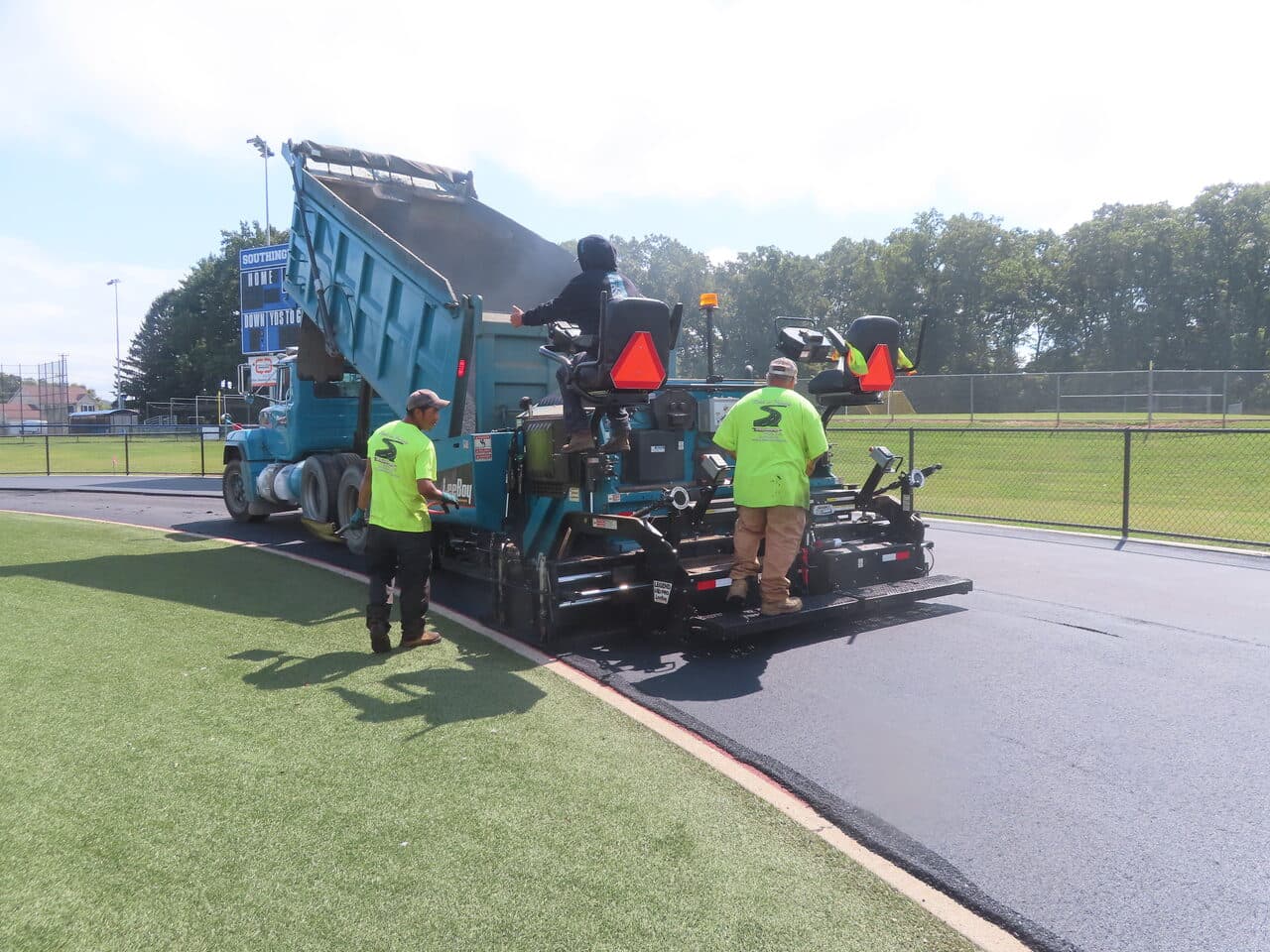 Athletic Surface Base Paving project in Southington, CT — paver and dump truck on track