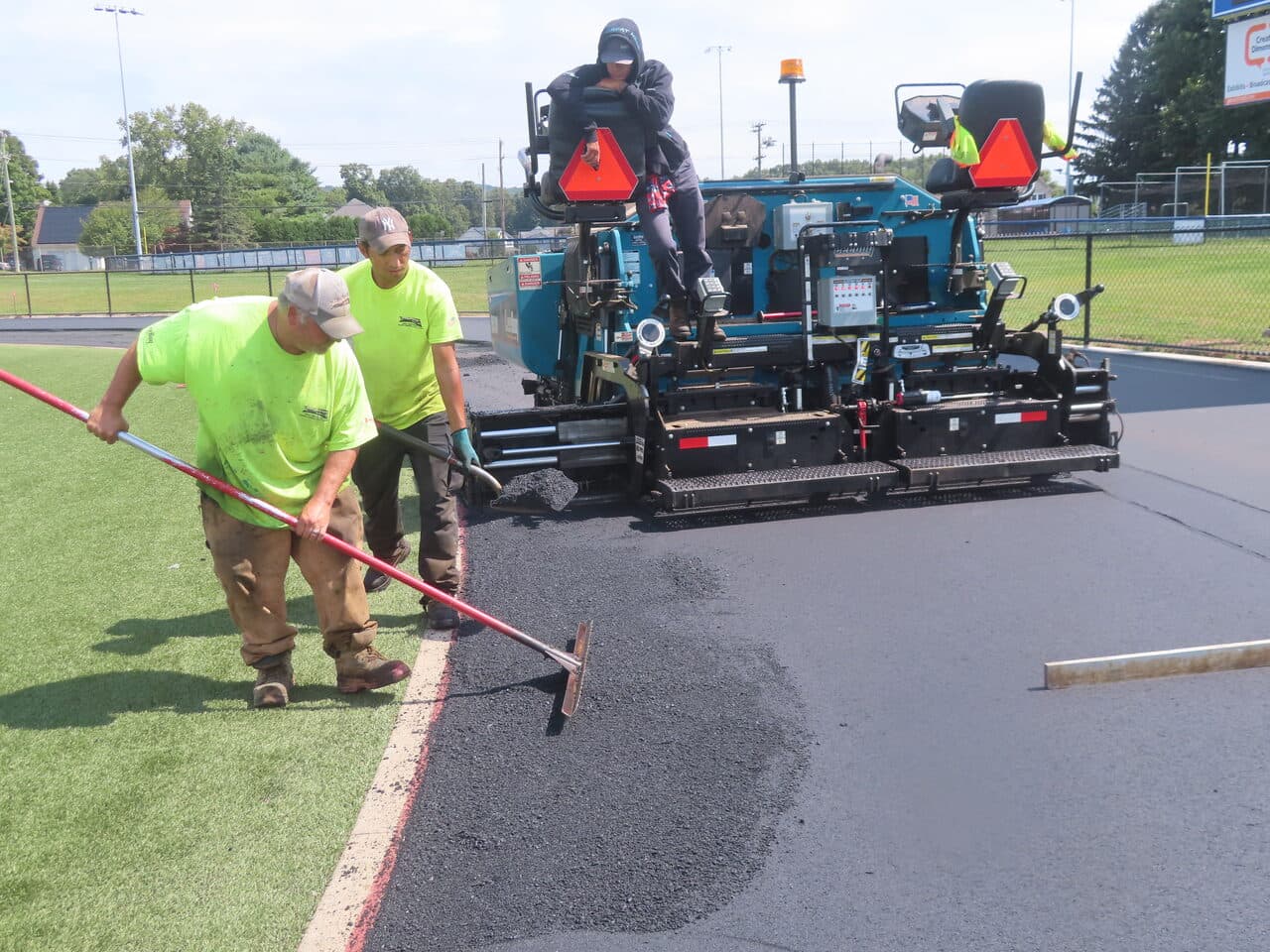 Athletic Surface Base Paving project in Southington, CT — paver and crew raking edge