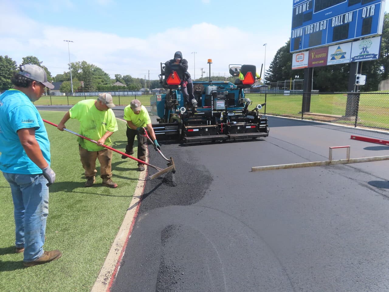 Athletic Surface Base Paving project in Southington, CT — crew raking near scoreboard