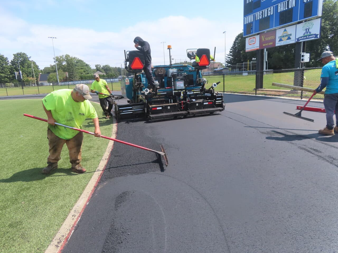 Athletic Surface Base Paving project in Southington, CT — paver with crew by scoreboard