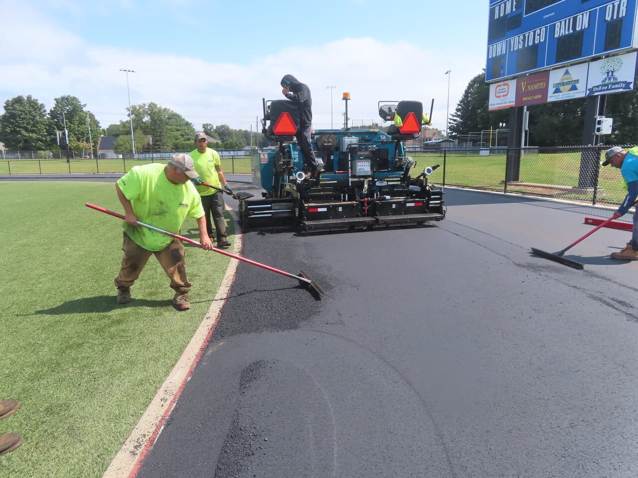 Athletic Surface Base Paving project in Southington, CT — paver and crew raking track