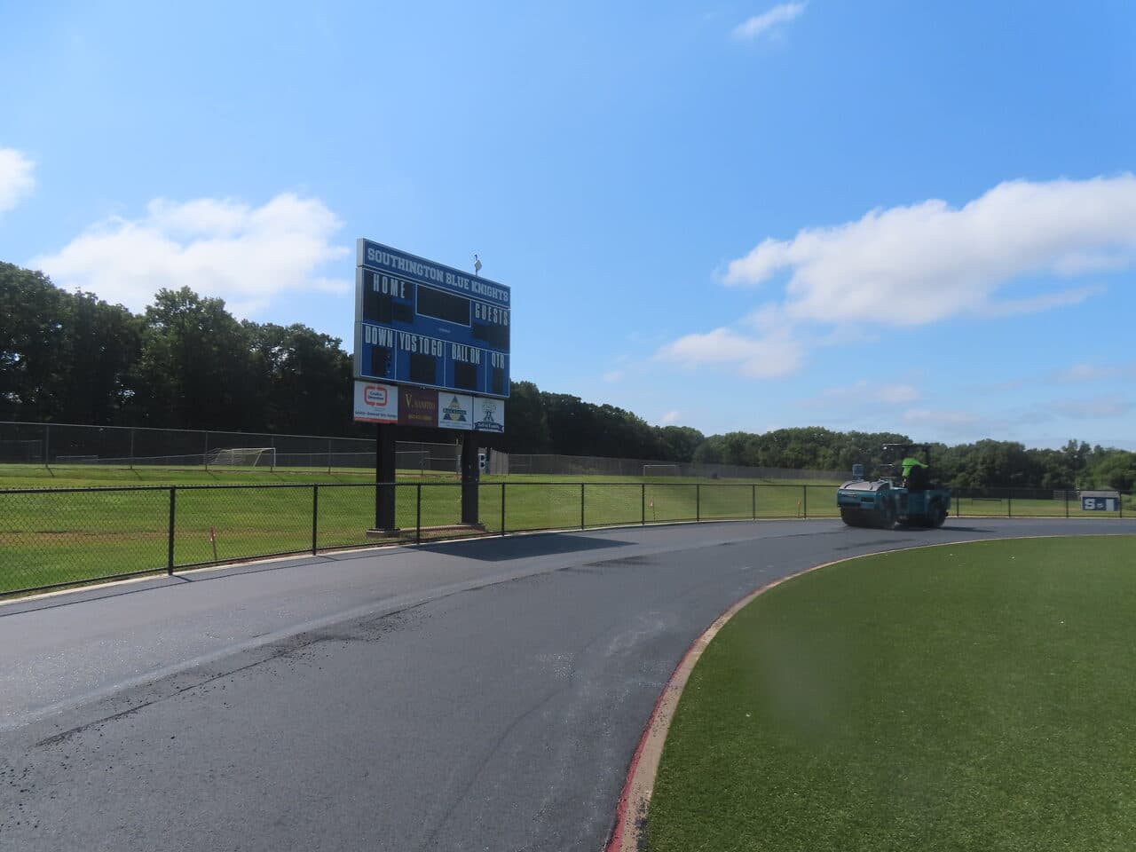 Athletic Surface Base Paving project in Southington, CT — finished track by scoreboard with roller