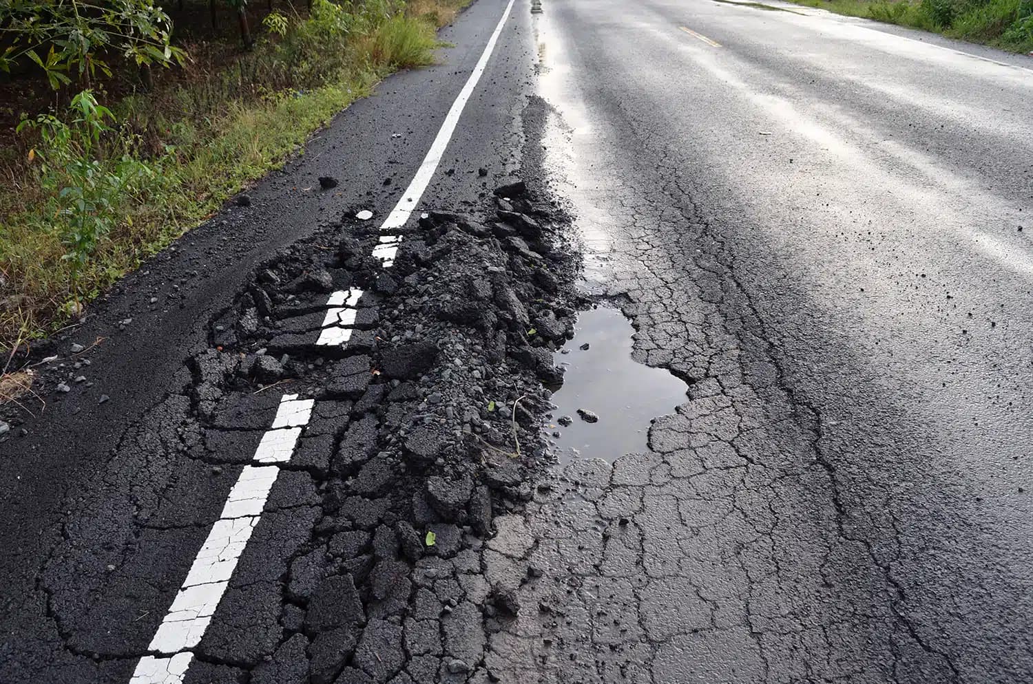 Severe asphalt rutting with pooled water on a damaged roadway curve