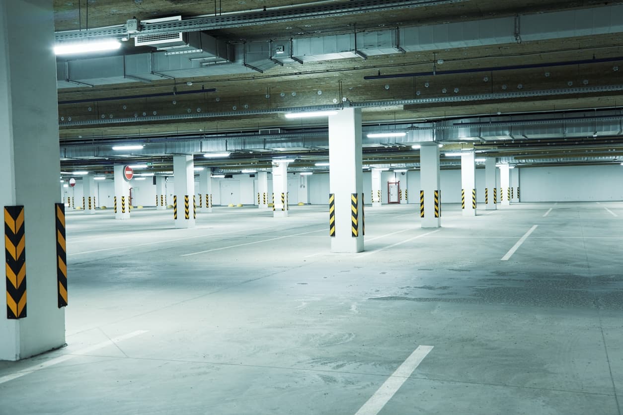 Indoor concrete parking structure with columns, lighting, and marked parking spaces showing a well-maintained commercial garage