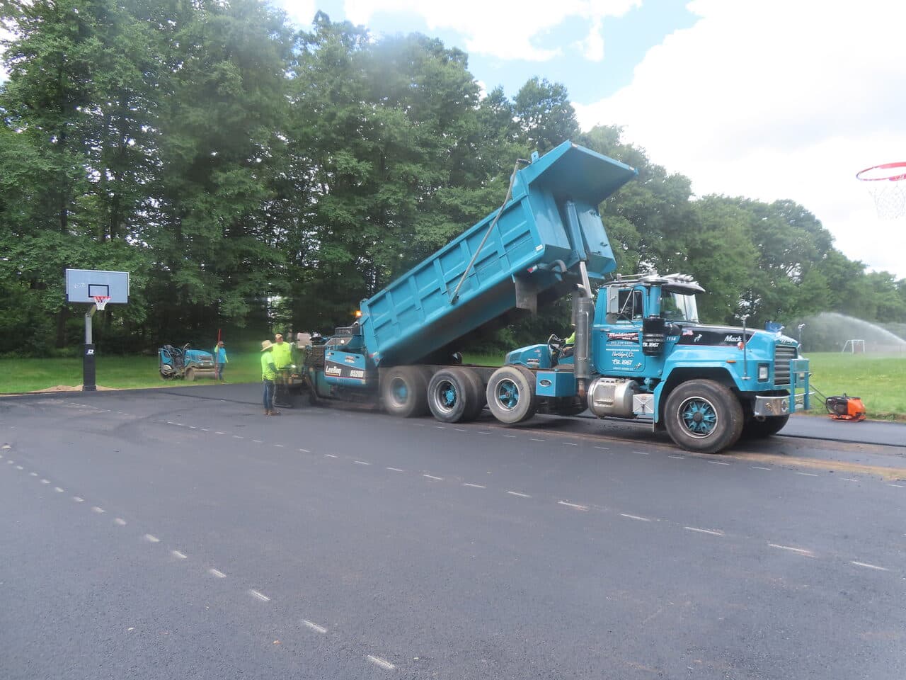 Parking Lot & Athletic Surface Base Paving project in East Hartford, CT — blue dump truck feeding paver