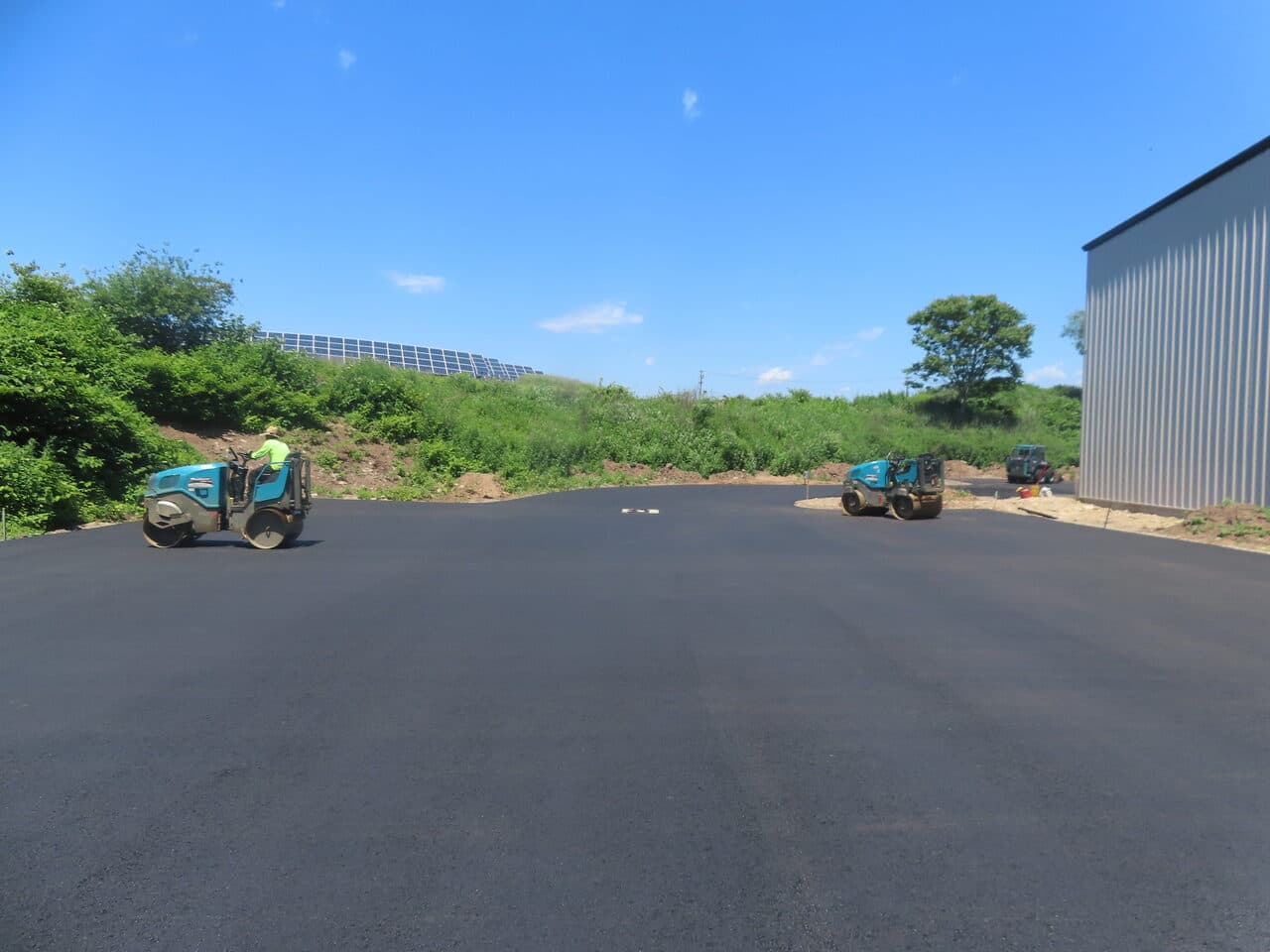 Finished commercial parking lot in East Haven, CT — fresh asphalt with rollers and clear blue sky