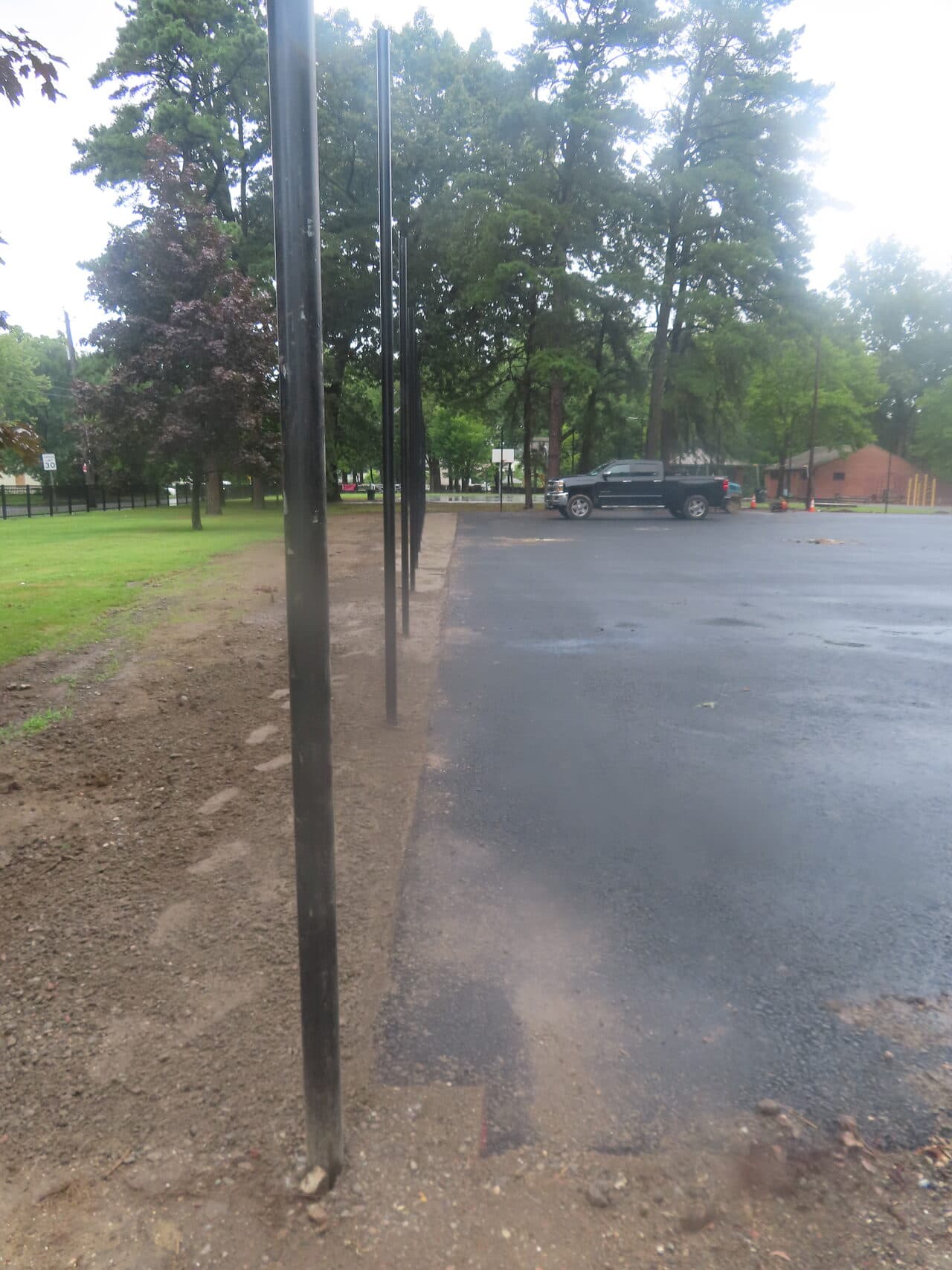 Asphalt Walkway Paving project in Springfield, MA — wet asphalt lot with fence posts