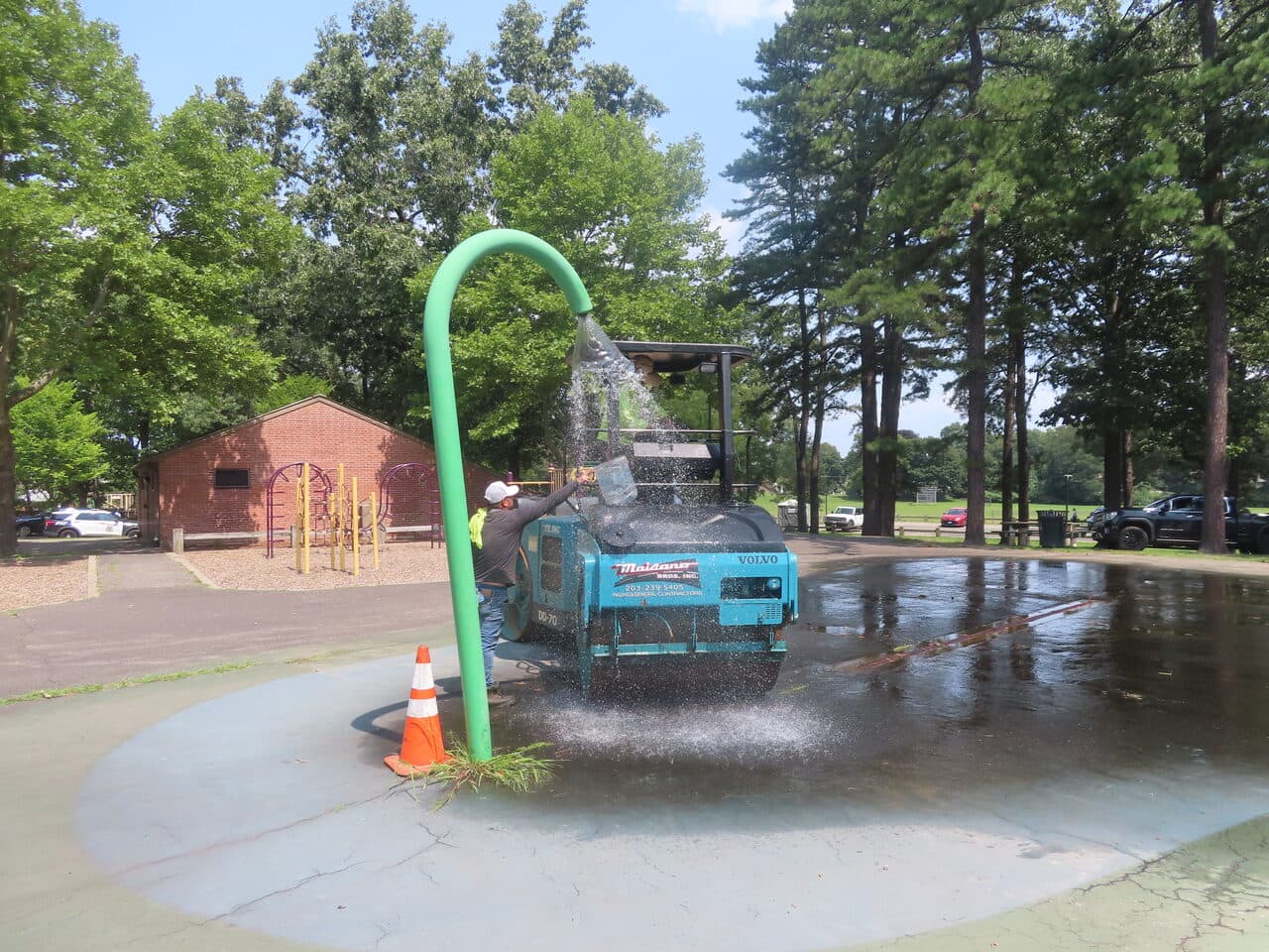 Commercial Parking Lot Paving project in Springfield, MA — worker rinsing roller near spray pad