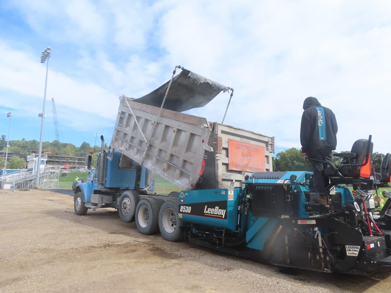 Athletic Surface Base Paving project in Burlington, VT — dump truck loading LeeBoy paver