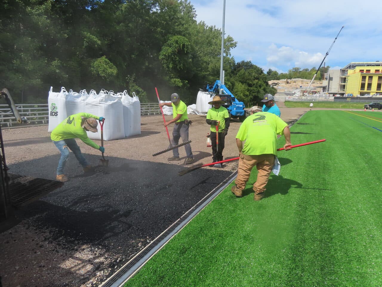 Athletic Surface Base Paving project in Burlington, VT — crew raking asphalt edge by turf