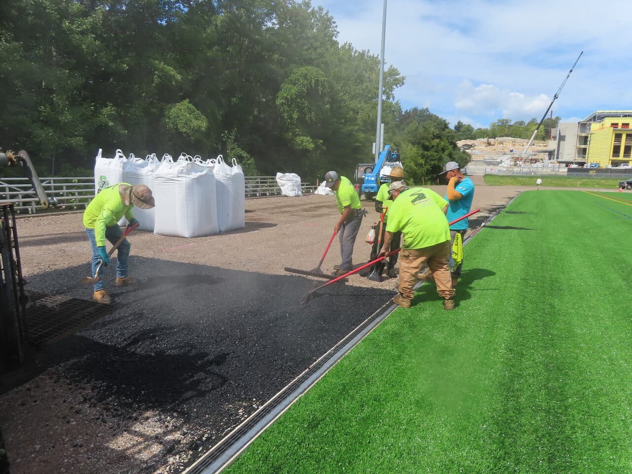Athletic Surface Base Paving project in Burlington, VT — crew spreading asphalt near turf