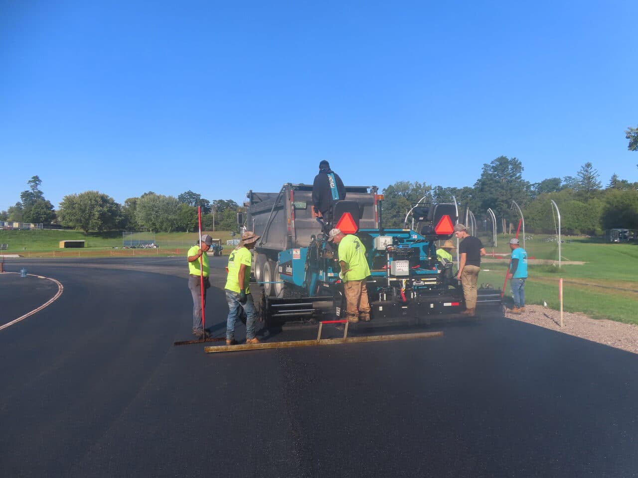 Athletic Surface Base Paving project in Burlington, VT — crew at paver on curved track