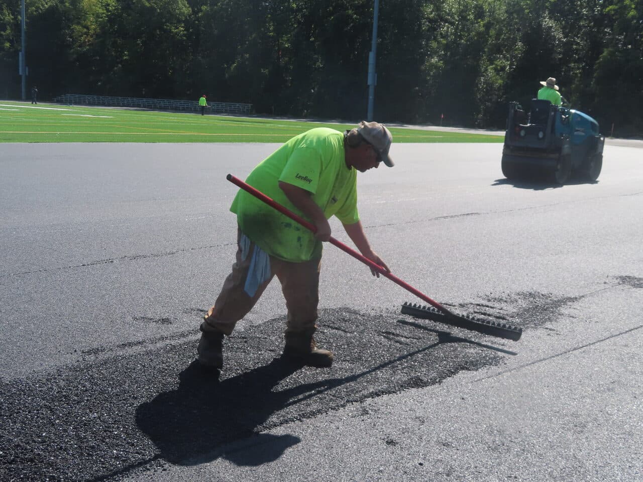 Athletic Surface Base Paving project in Burlington, VT — worker raking asphalt near field