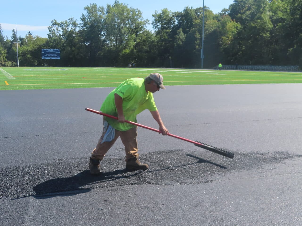 Athletic Surface Base Paving project in Burlington, VT — worker raking asphalt patch