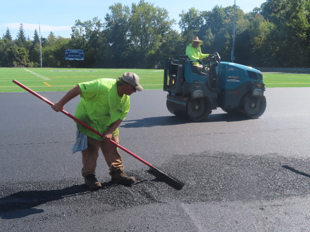 Athletic Surface Base Paving project in Burlington, VT — worker raking with roller behind