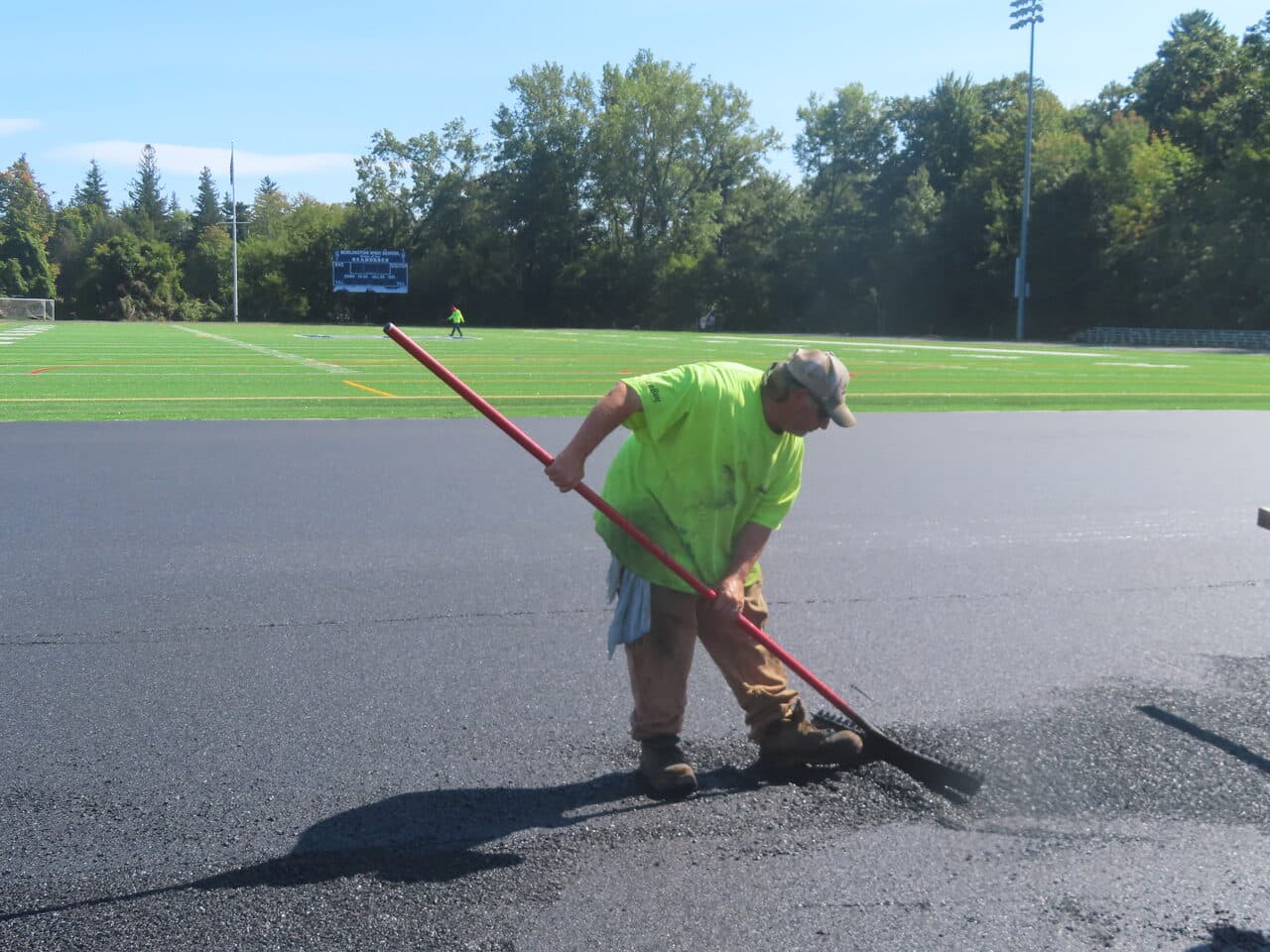 Athletic Surface Base Paving project in Burlington, VT — worker raking asphalt by field