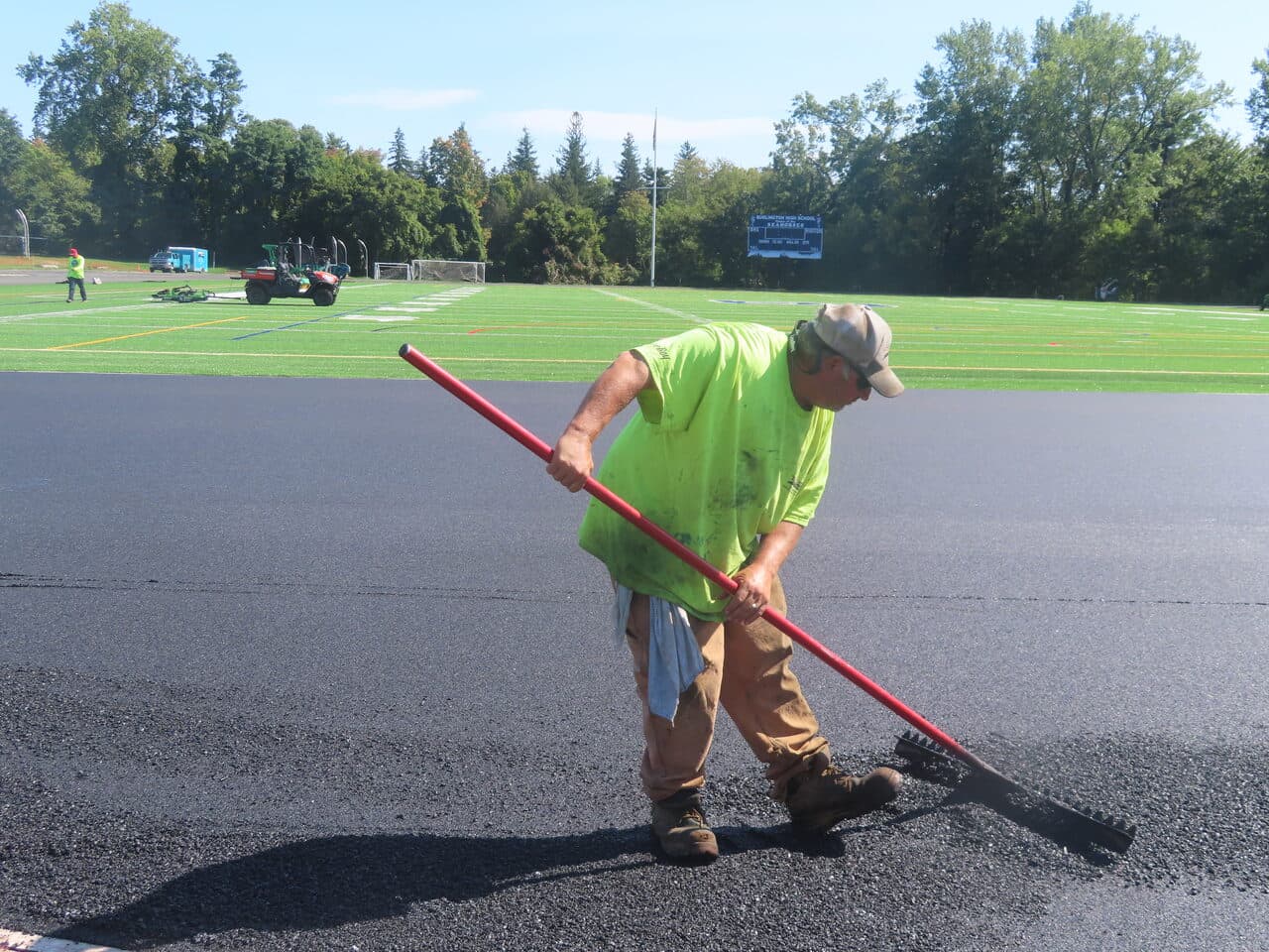 Athletic Surface Base Paving project in Burlington, VT — worker raking fresh asphalt