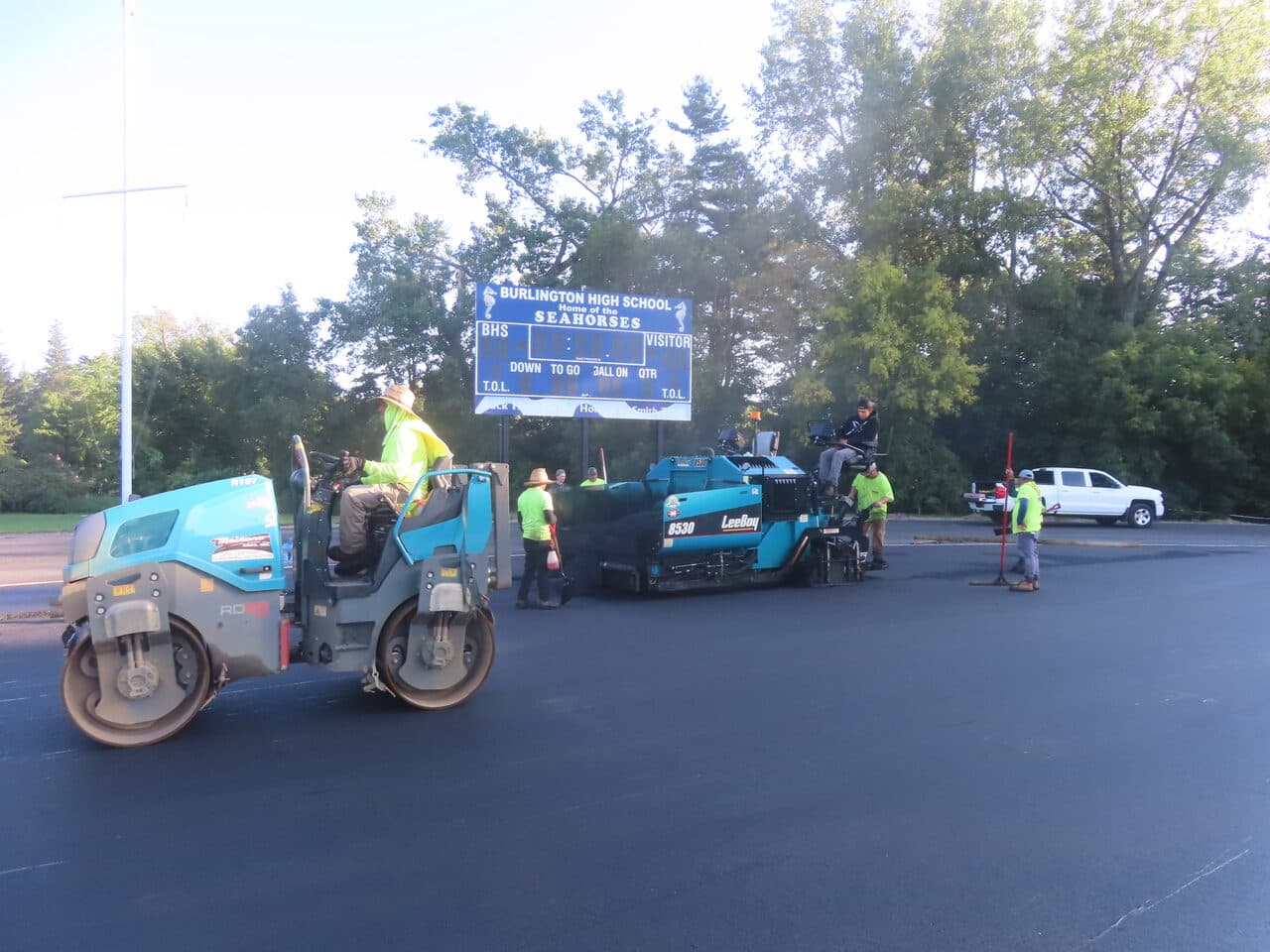 Athletic Surface Base Paving project in Burlington, VT — roller and paver by scoreboard