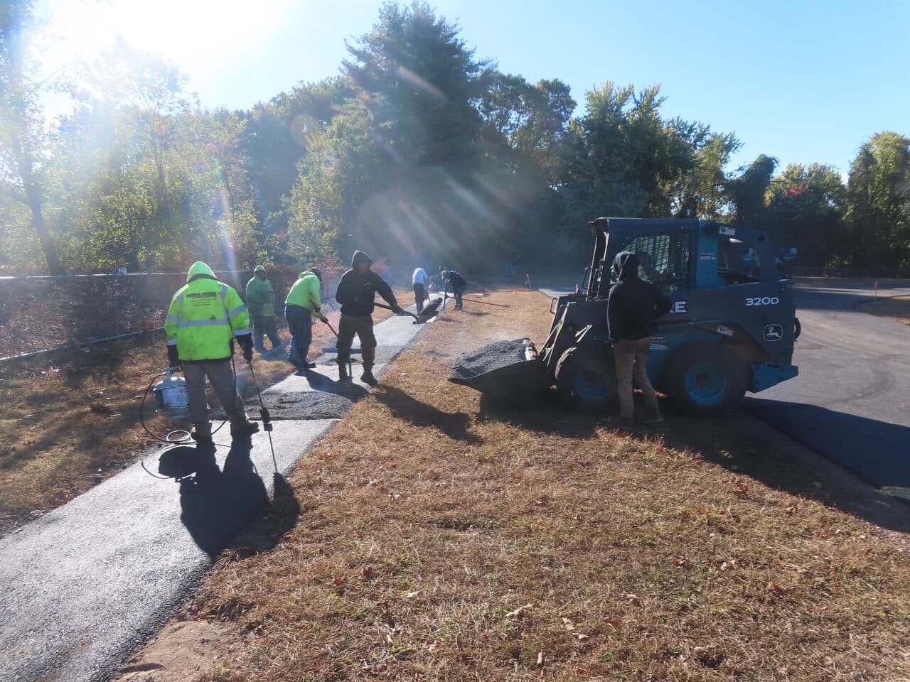 Athletic Surface Base Paving project in East Windsor, CT — crew paving track edge with skid steer