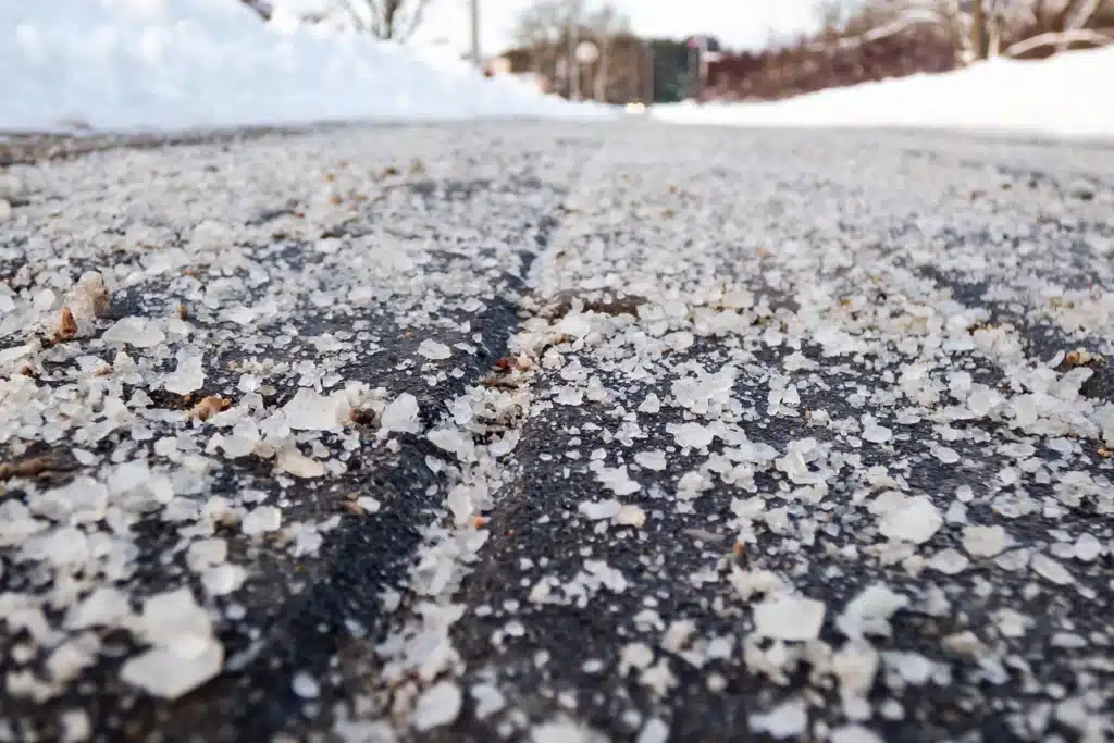 Rock salt scattered across an asphalt driveway during winter to melt ice and improve traction.