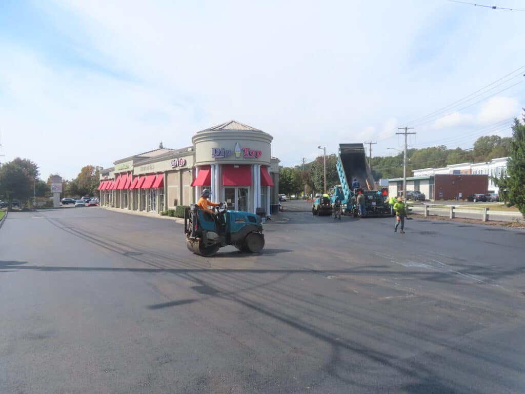 Commercial paving crew resurfacing a shopping plaza parking lot.