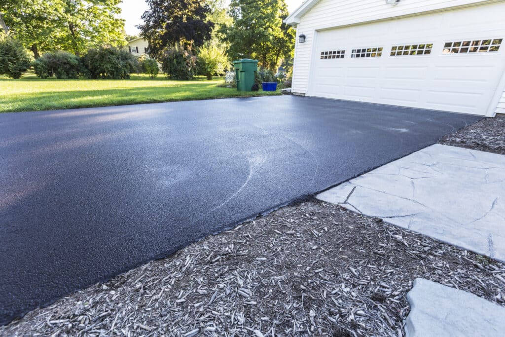 Freshly paved residential asphalt driveway in front of a white garage, illustrating the benefits of local asphalt production.
