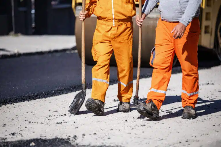 Asphalt paving crew in safety gear and heavy-duty boots standing on freshly laid pavement