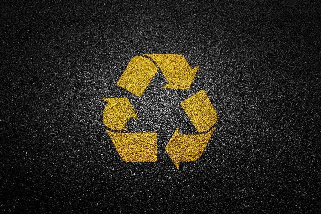 Yellow recycling symbol painted on asphalt pavement