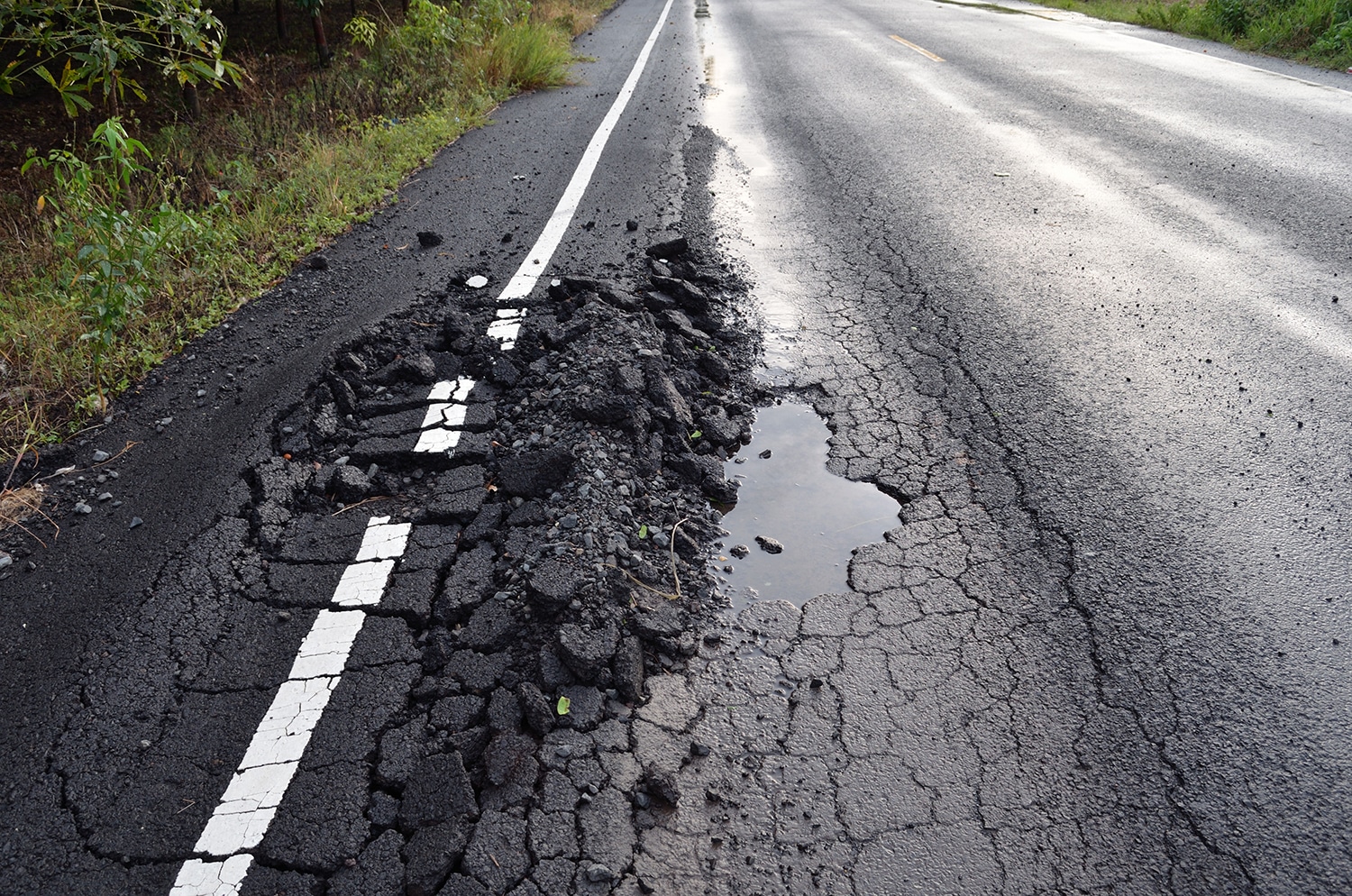 Severe asphalt rutting with pooled water on a damaged roadway curve