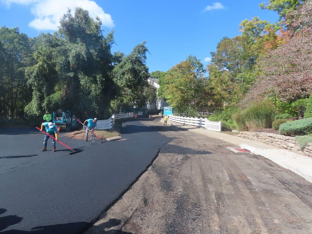 Asphalt paving underway on a residential roadway in Bethany, CT by Maisano Bros. Inc., with fresh pavement installation and hand finishing in progress.