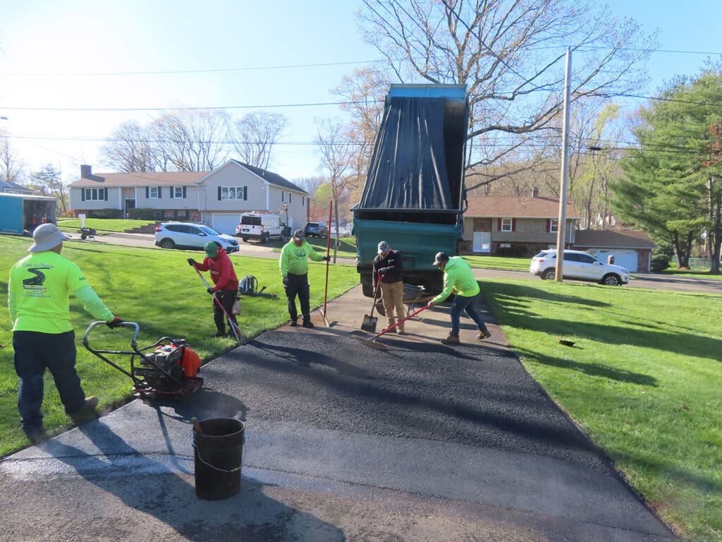 Workers paving a residential driveway in Vernon, CT on a sunny day.